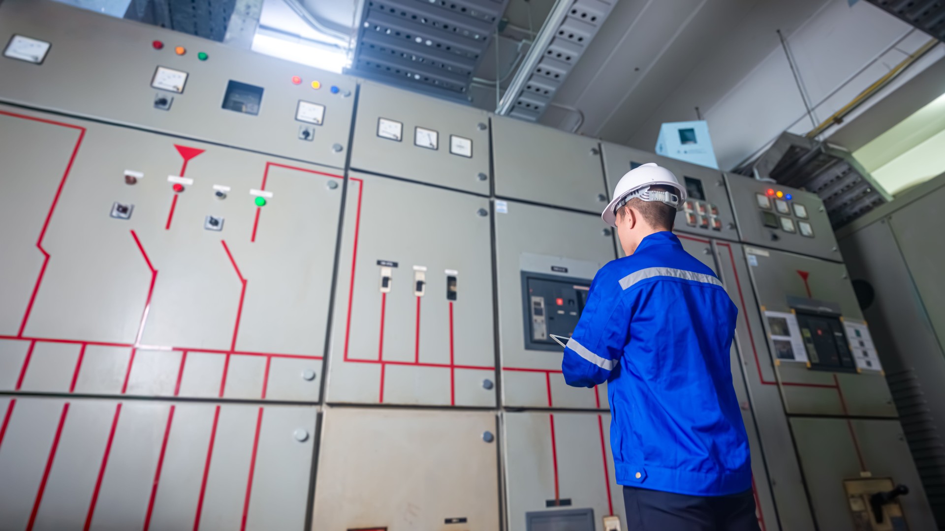 Electrical engineers check the operation of the main electrical control panels and switches, record values on tablets, electrician inspect the electrical systems in the factory.